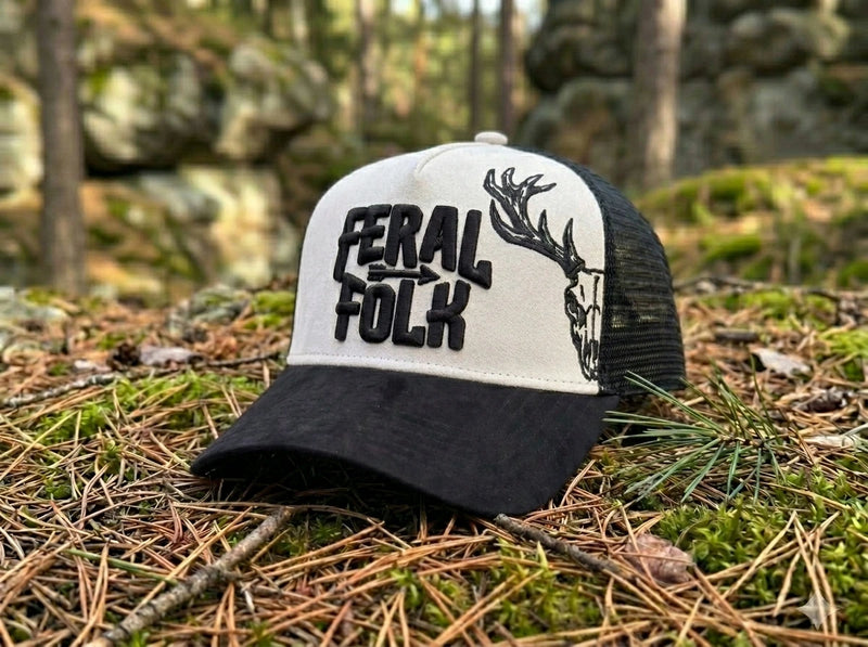 Black and light grey cap with 'Feral Folk' text and deer design on a forest floor.